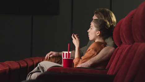 side view of couple hugging sitting in the cinema while they watching a movie and eating popcorn