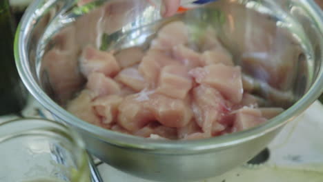 Pouring-salt-on-small-pieces-of-chicken-breast-in-bowl-on-picnic-table-outside