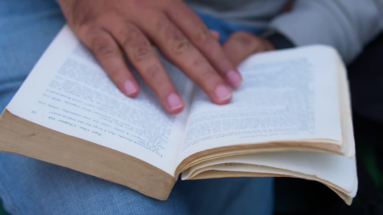 gusano de libro masculino disfrutando de la naturaleza mientras lee y da la vuelta a la página, joven hombre del sur de asia absorto en la lectura al aire libre
