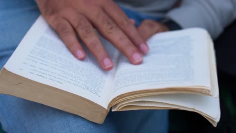 Ratón-De-Biblioteca-Masculino-Disfrutando-De-La-Naturaleza-Mientras-Lee-Y-Pasa-La-Página,-Joven-Del-Sur-De-Asia-Absorto-En-La-Lectura-Al-Aire-Libre