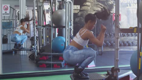 sexy culturista latina saltando sentadillas en el gimnasio con un espejo en el fondo