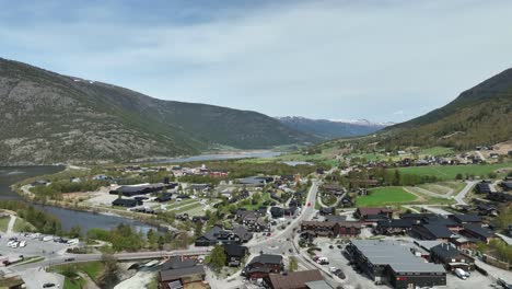 rising aerial revealing beautiful lom and fossbergom in norway - stunning landscape with busy street and snow capped mountain background