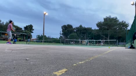 Zwei-Männliche-Freunde-Spielen-Auf-Dem-Tennisplatz,-Sport,-Mit-Lichtern,-Die-In-Die-Nacht-Eintreten