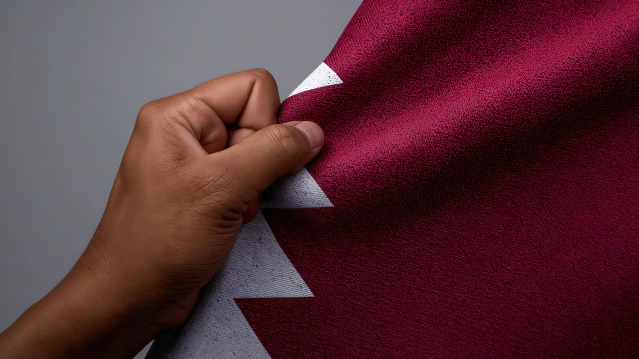 Entering left, right hand pinching-pulling maroon cloth with white zigzag at studio, showing weave