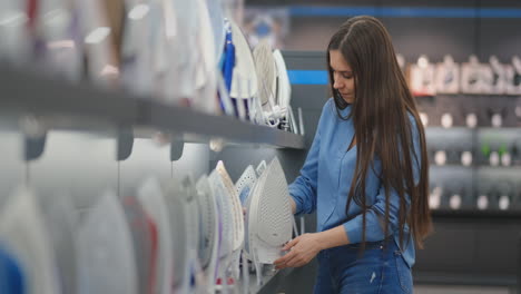 beautiful brunette woman chooses an iron in a consumer electronics store