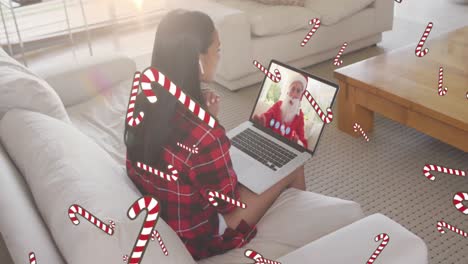 Animation-of-candy-canes-over-mixed-race-woman-on-laptop-video-call-with-santa-claus-at-christmas