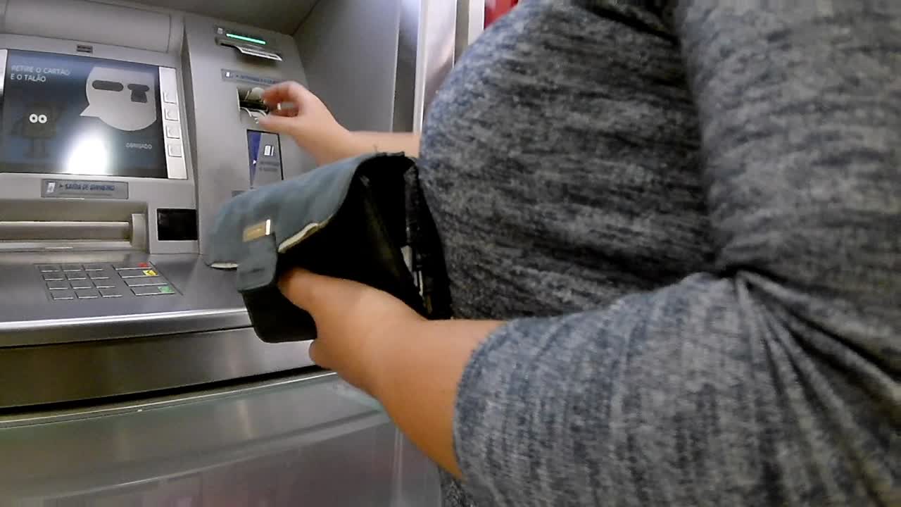 Woman operating a ATM automated teller machine, end of operation, she takes out her card and receipt and packs it away in her purse
