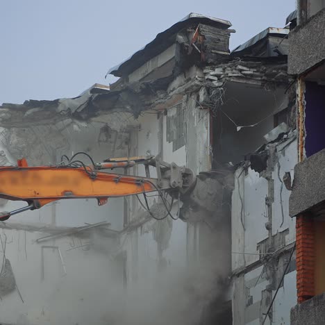 destruction of the premises ruined by an earthquake. demolishing equipment is breaking the upper floors. dusty cloyds rise in the air