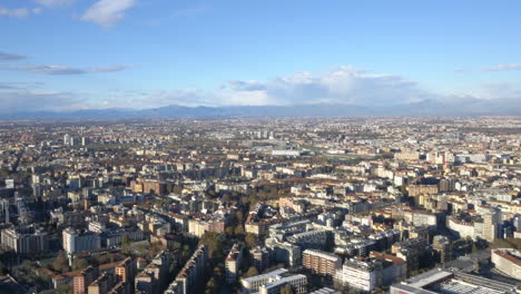 vast city of milan with mountain range of alps in far distance, aerial view