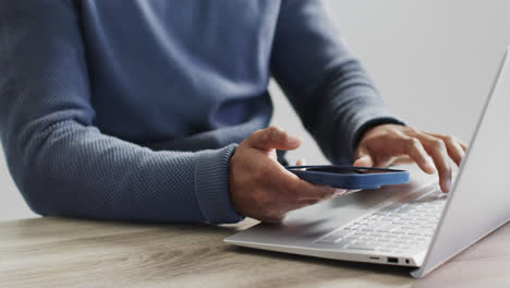 video of biracial businessman using laptop and smartphone on white background