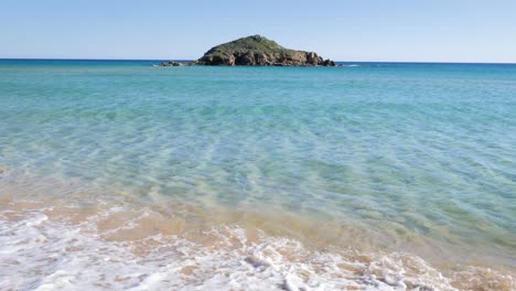 aguas turquesas claras y poco profundas con una pequeña isla rocosa en el horizonte en el sur de cerdeña, italia