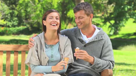 una joven pareja comiendo helado en un banco del parque