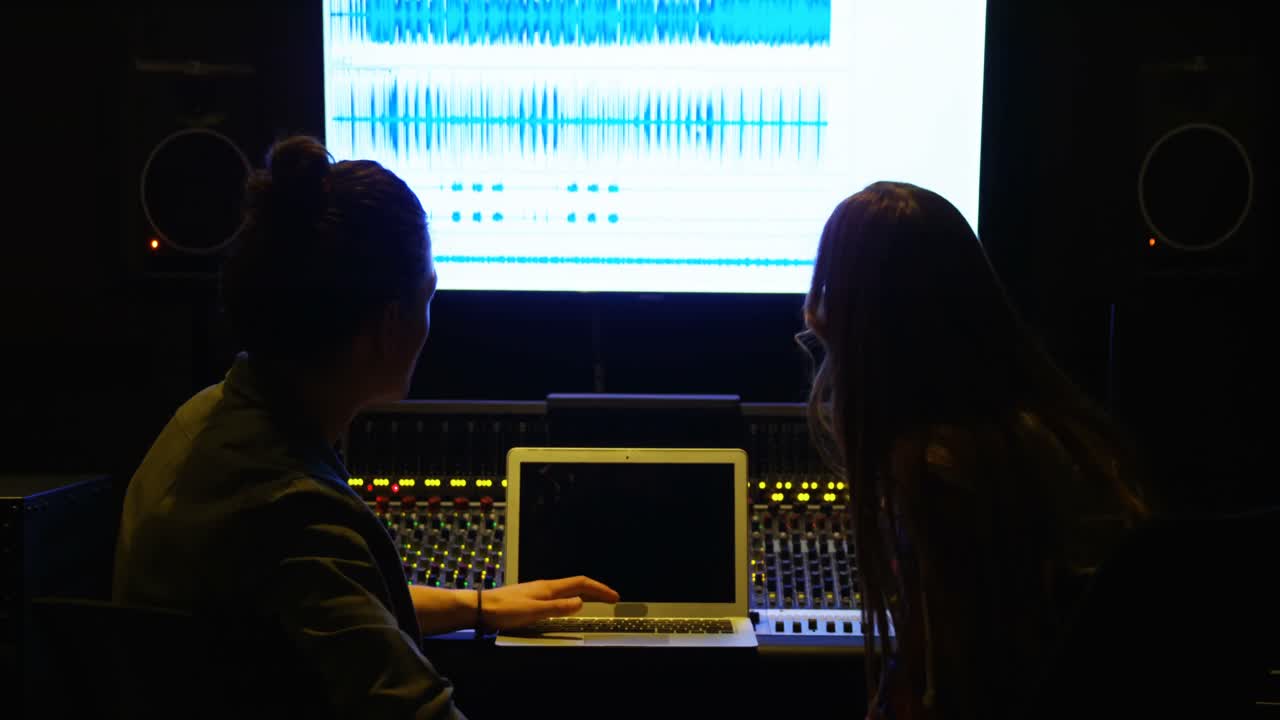 Audio engineers using laptop while mixing sound