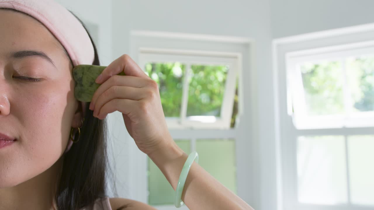 African American woman at vanity starting gua sha, lifting and massaging under-eye to jaw depuffing