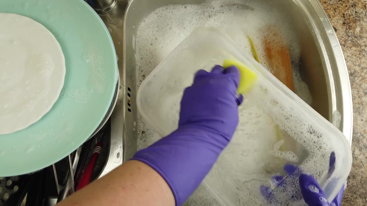 Una donna lava i piatti sotto un getto d'acqua.