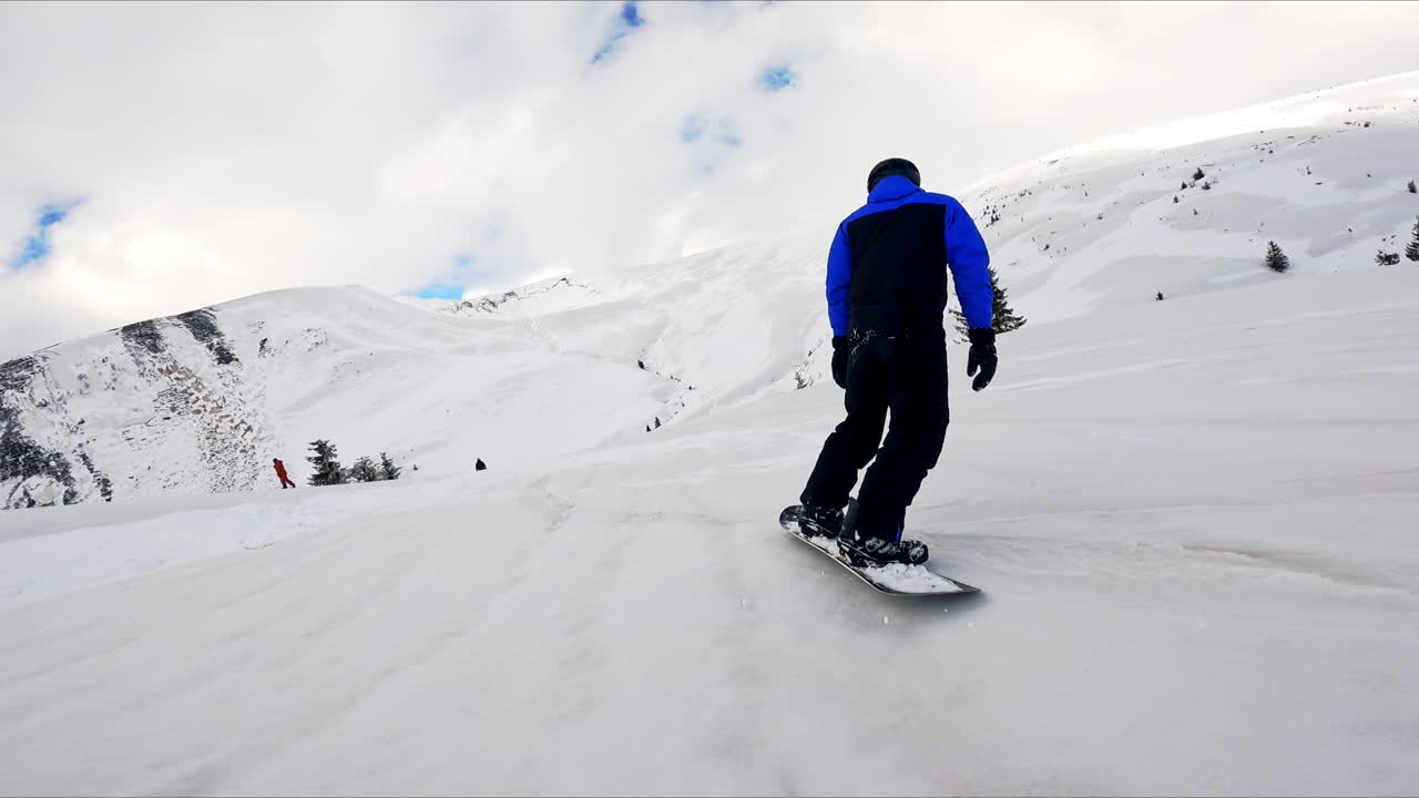 Following a male snowboarder going down the slope. Winter sport activity in the mountains.