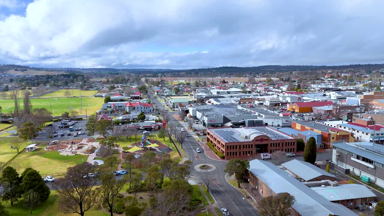Drone footage glides above a suburban road in Armidale, New South Wales, revealing commercial buildings, green spaces, and overcast winter lighting