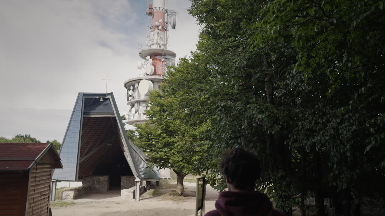 молодой турист идет к коттеджу "маунтэн" и радиовышке среди высоких деревьев.