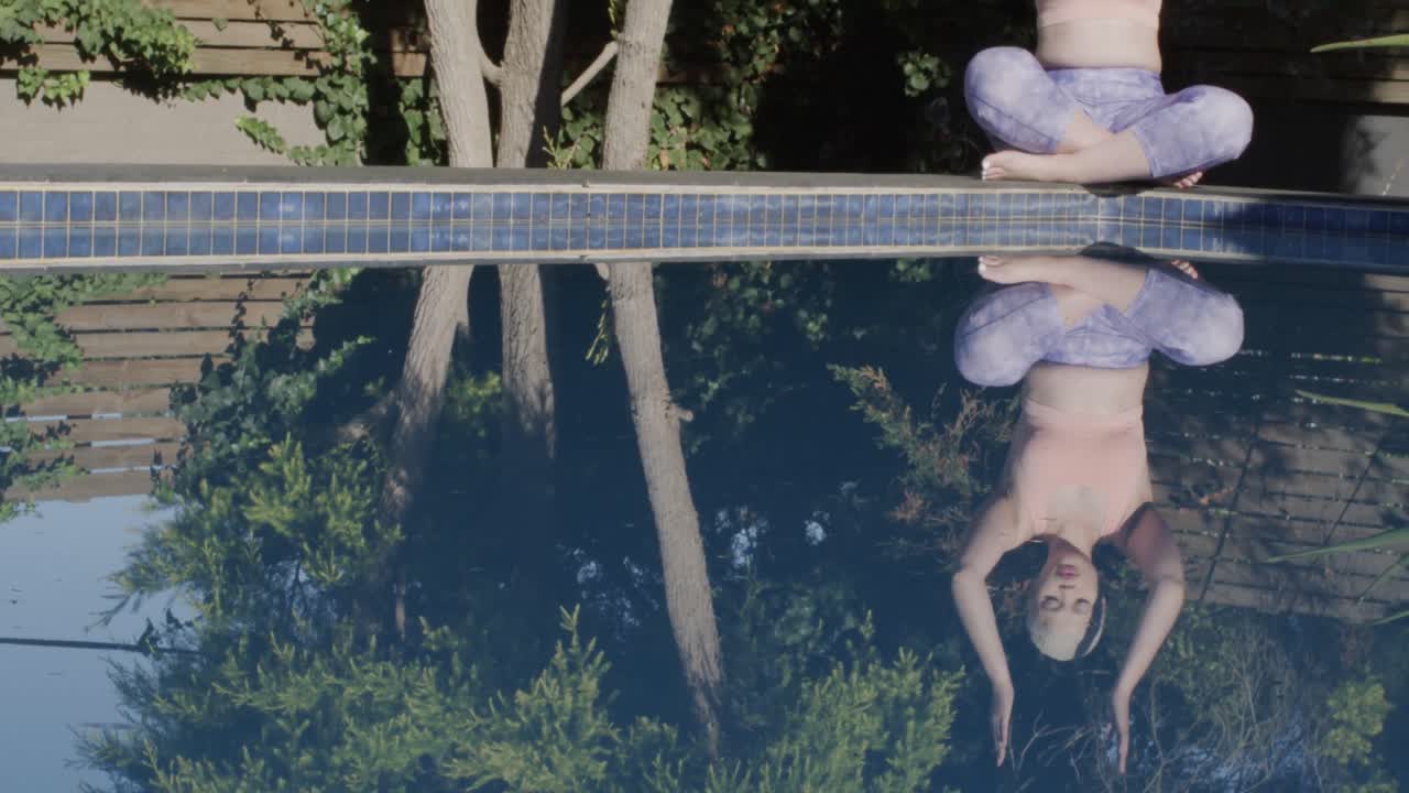 요가 를 연습 하고 천천히 움직이는 정원 에 있는 수영장 에서 명상 하는 두 인종 의 여성 에 초점을 맞추었다