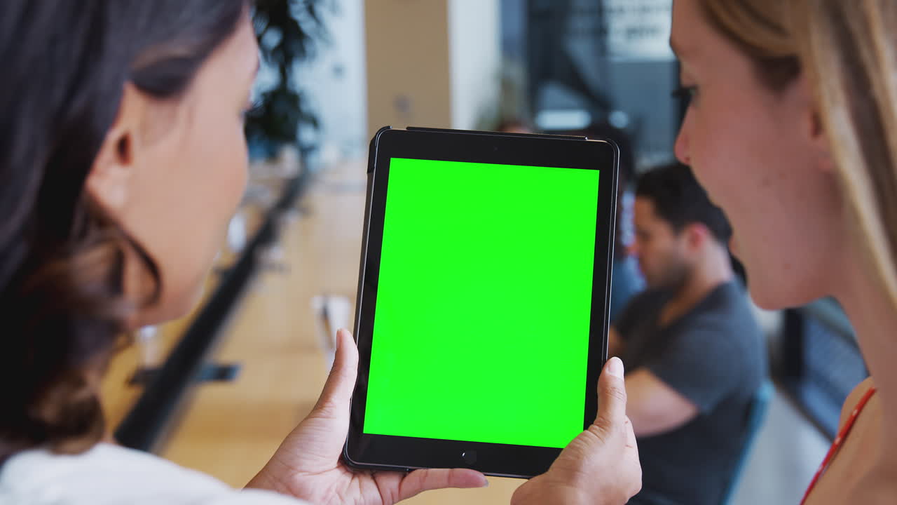 Close Up Of Two Businesswomen Looking At Blank Digital Tablet With Green Screen In Shared Office