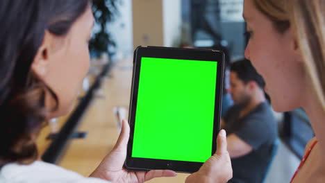 cerca de dos mujeres de negocios mirando una tableta digital en blanco con pantalla verde en una oficina compartida