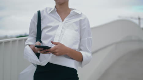 una mujer de negocios desconocida enviando mensajes en su teléfono inteligente caminando por la calle de la ciudad de cerca.