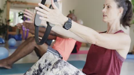 diverse seniors holding rings exercising with female pilates coach, unaltered, in slow motion