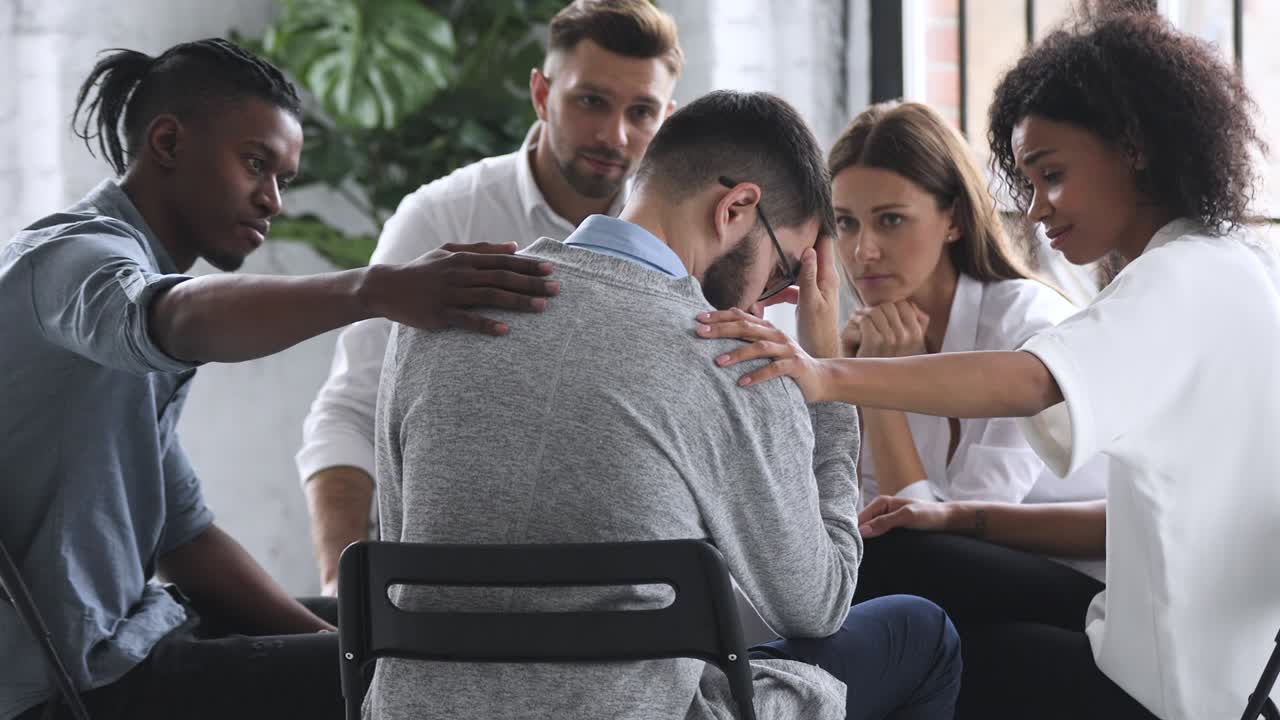 jóvenes de raza mixta diversas personas compasivas apoyando a un hombre desesperado y infeliz.