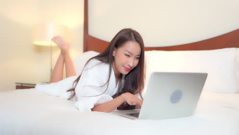 Feliz-Joven-Asiática-En-El-Dormitorio-Con-Laptop,-Chat-En-Redes-Sociales-Con-Amigos-A-Cámara-Lenta-Full-Frame