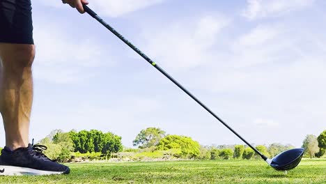 close-up of golfer's legs and club preparing to hit a ball on a sunny day.