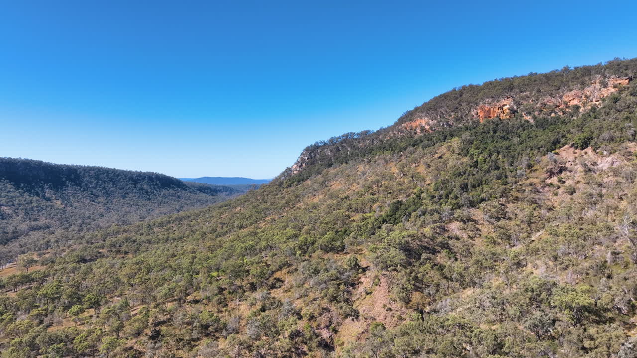 deslizamientos aéreos a través de los flancos boscosos de las montañas del parque nacional de cania, destacando franjas de verdes más profundos, acantilados escarpados y cielos azules radiantes