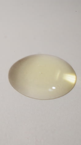 golden drop of fresh jojoba oil falls spreading on plain white surface. transparent liquid used for organic facial cosmetic products macro