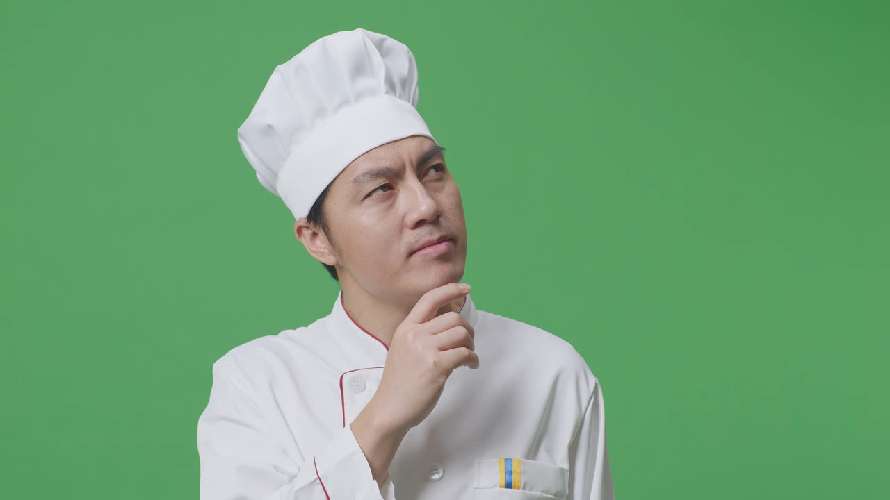 Close Up Of Asian Man Chef Thinking And Looking Around Then Raising His Index Finger While Standing In The Green Screen Background Studio