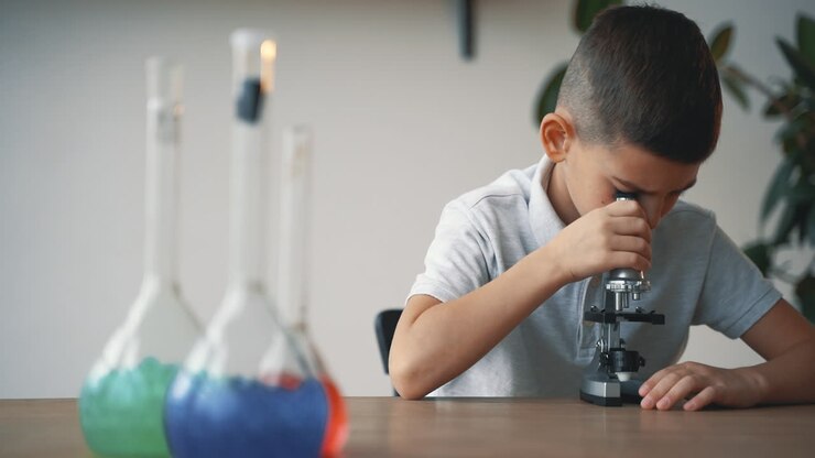Menino com vidraria de laboratório e um microscópio. Crianças e ciência