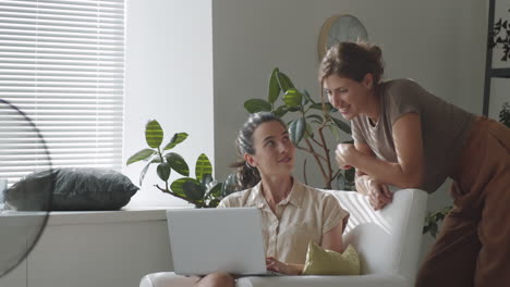 dos mujeres usando computadora portátil y hablando en casa
