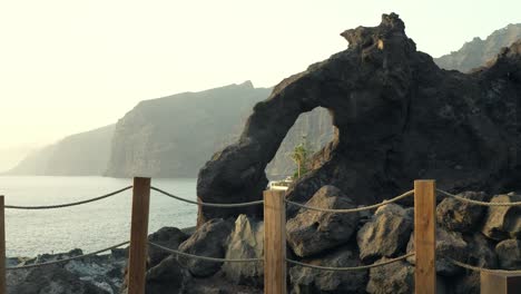 Pan-across-scenic-coastal-sea-cliffs-and-rock-arch-along-Los-Gigantes-promenade,-Canary-Islands-Spain