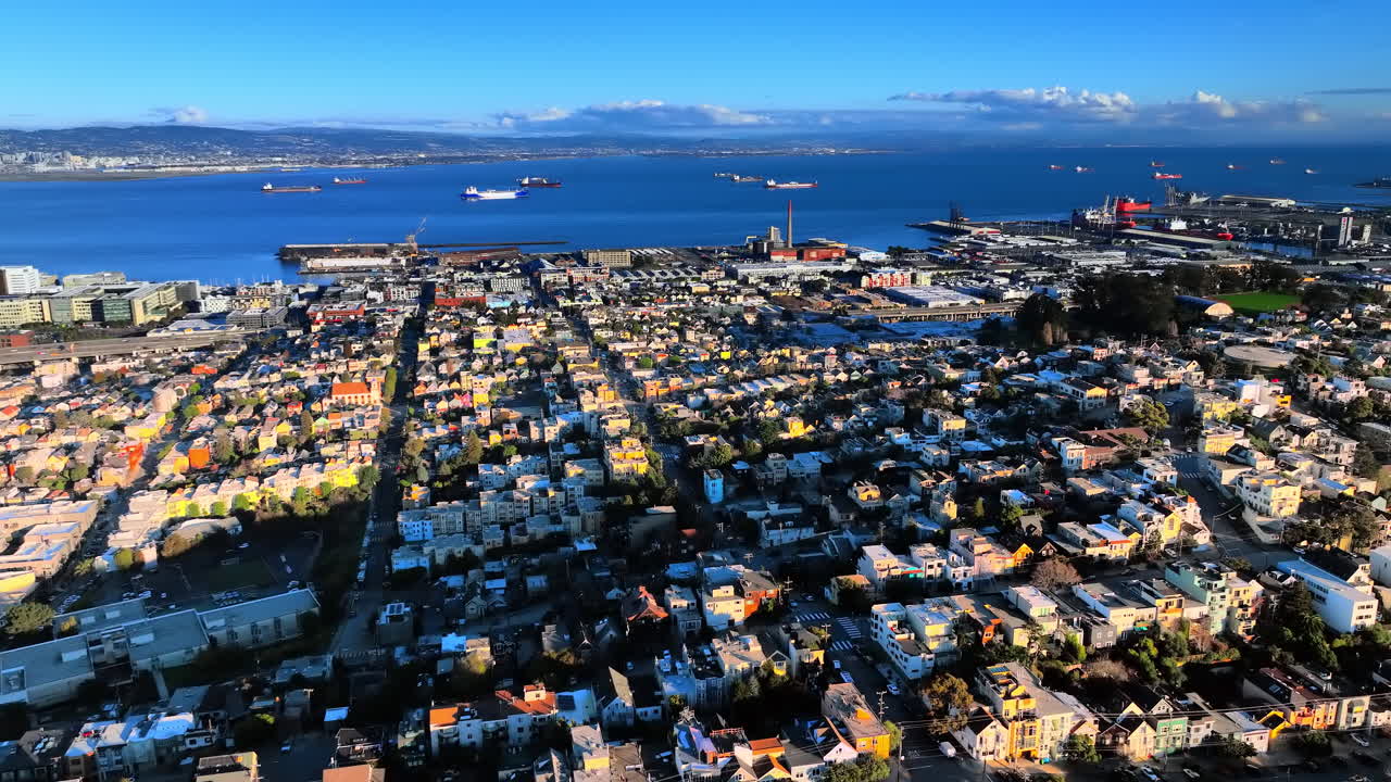 Ripresa aerea di case residenziali colorate in primo piano con un porto industriale, navi da carico e la baia sullo sfondo. Area industriale costiera e case residenziali a San Francisco.