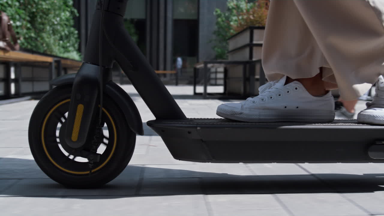 白いスニーカーでキックスクーターに乗る女性の足元。都会の旅人コンセプト