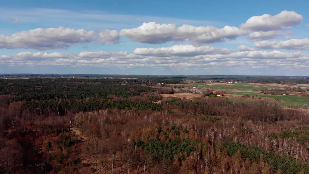 Drone pans across thick forest and farmland in countryside under fluffy white clouds