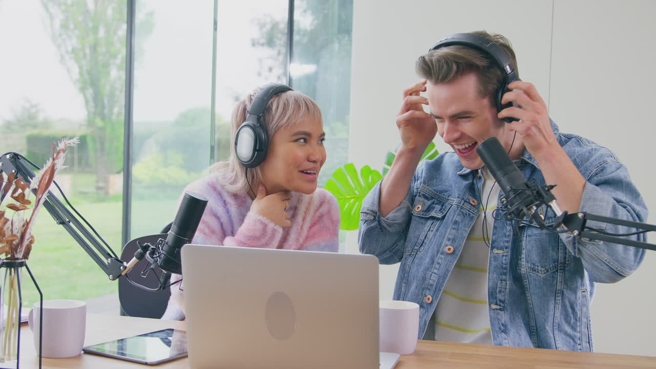 Couple With Laptop And Digital Tablet Wearing Headphones Vlogging With Microphone Live Streaming