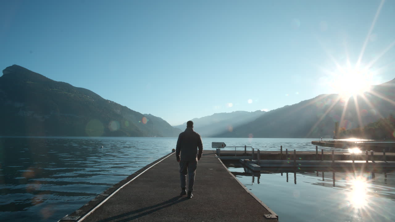 Man walking to the sharp corner of boat pier in Faulensee Switzerland and watching over the morning valley to Sun.