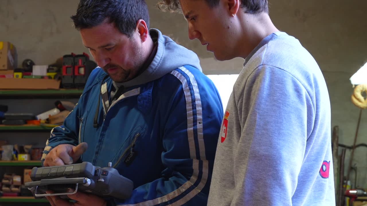 Close up of young and adult farmers jointly operating a drone controller inside a barn environment
