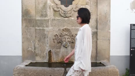 woman walking in monsanto village with old fountain in background, portugal