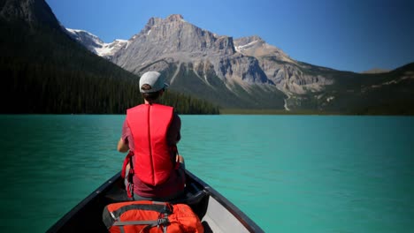 Rear-view-of-young-caucasian-man-rowing-boat-on-a-turquoise-river-in-the-sunshine-4k