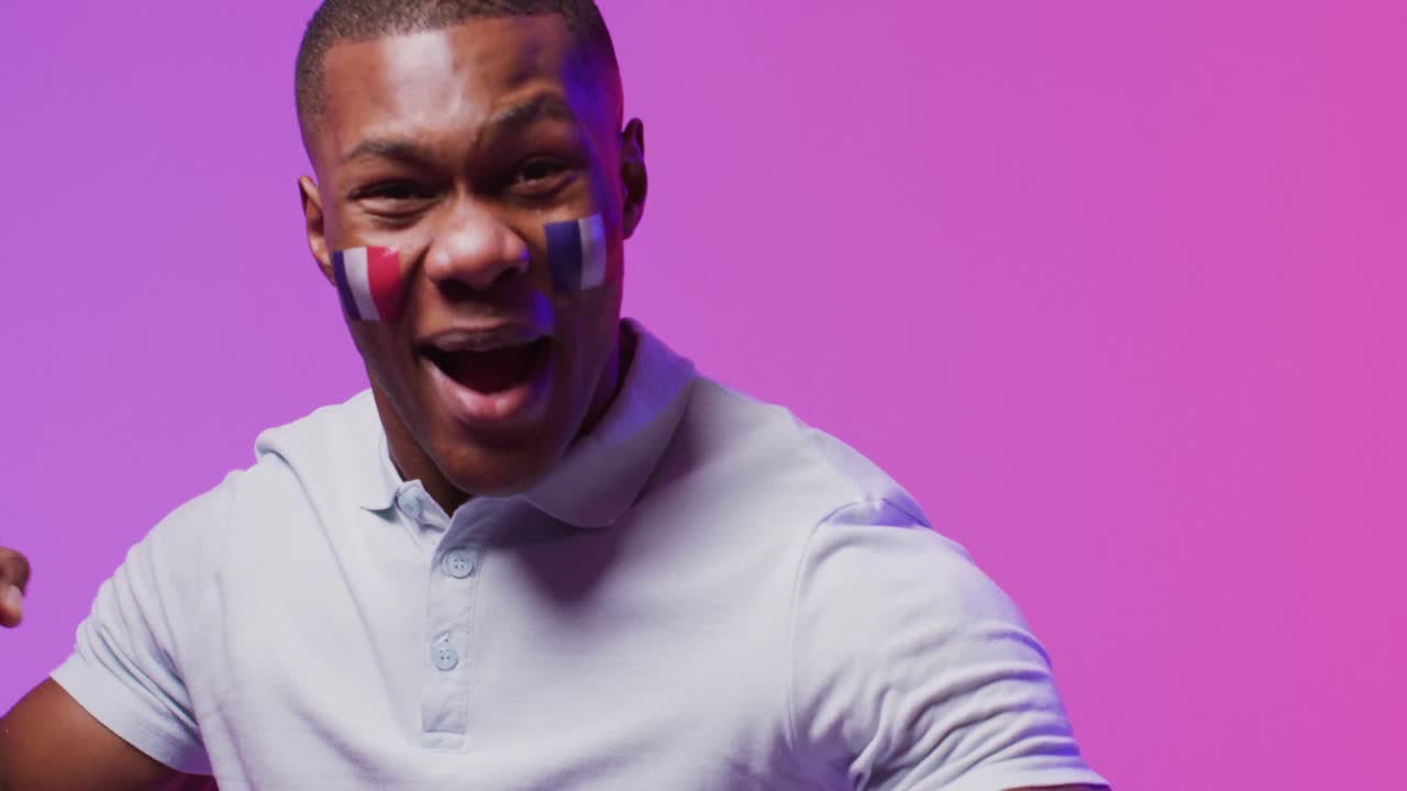 Portrait of happy african american male football supporter with flag of france over pink lighting