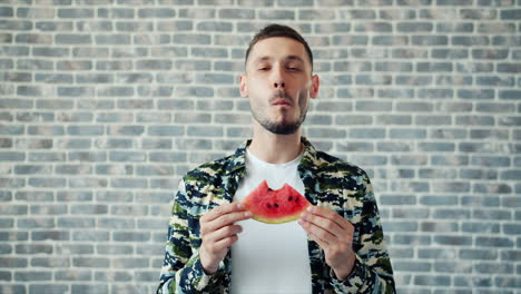 man eating watermelon slice in front of brick wall
