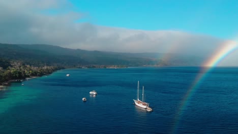 Rainbow-Over-Sailboat-and-Boats-in-Tropical-Sea-Gulf,-Aerial-View-of-Coastline-of-Exotic-Island