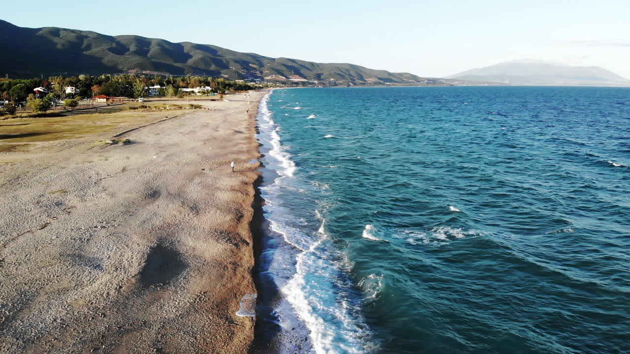 View of Aegean sea coast in Asprovalta at sunset from the drone. People on the beach. Rough sea, waves with foam. Greece