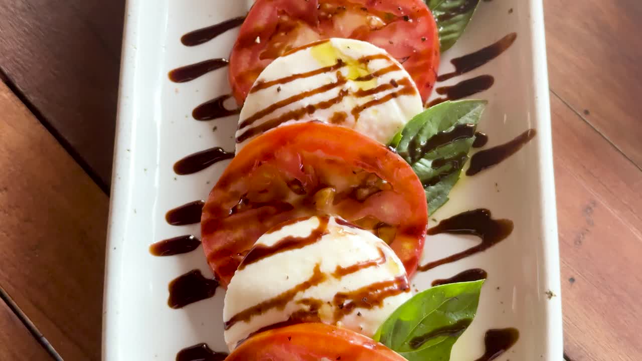 Fresh Caprese salad with tomatoes, mozzarella, basil, and balsamic glaze on a wooden table in natural light