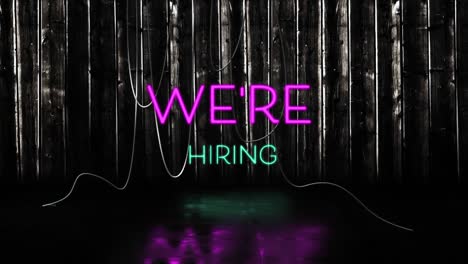 Animation-of-we're-hiring-text-in-pink-and-blue-neon-letters-on-black-background